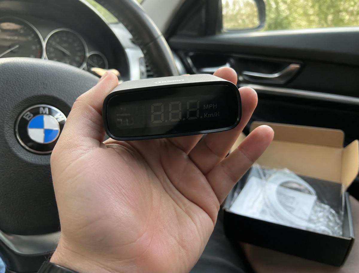 Boîtier MasterHUD Pro tenu dans la main devant le volant d'une voiture